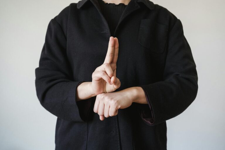 A person in a black coat demonstrating a sign language gesture indoors.