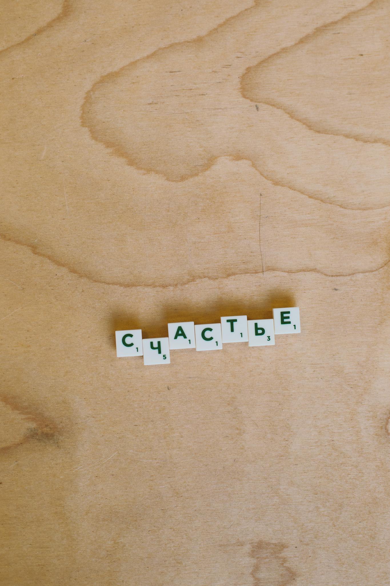 Cyrillic Scrabble tiles spelling 'happiness' on a wooden surface, conceptual design.